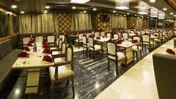 A spacious restaurant with multiple dining tables and booths, marble flooring, and a decorative wall with a dragon mural.