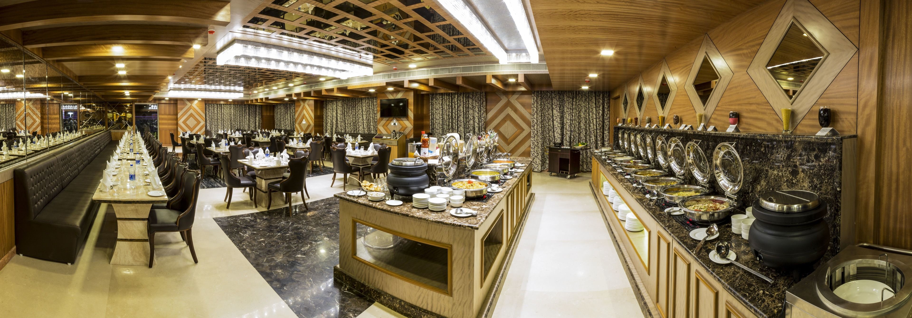 Un comedor de hotel con varias mesas, una barra de buffet y una larga barra con distintos alimentos.