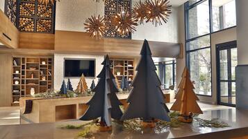Un intérieur moderne avec un comptoir d’accueil en bois, des sapins de Noël et une grande fenêtre laissant entrer la lumière naturelle.