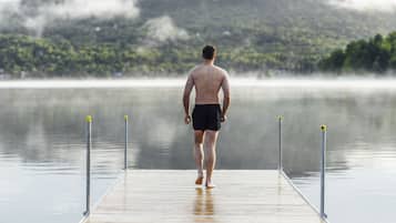 Un homme marchant sur une jetée en bois, avec une chaîne de montagnes brumeuses en arrière-plan.