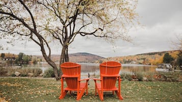 Deux chaises Adirondack rouges, placées face à un lac, avec un arbre et des collines en arrière-plan.