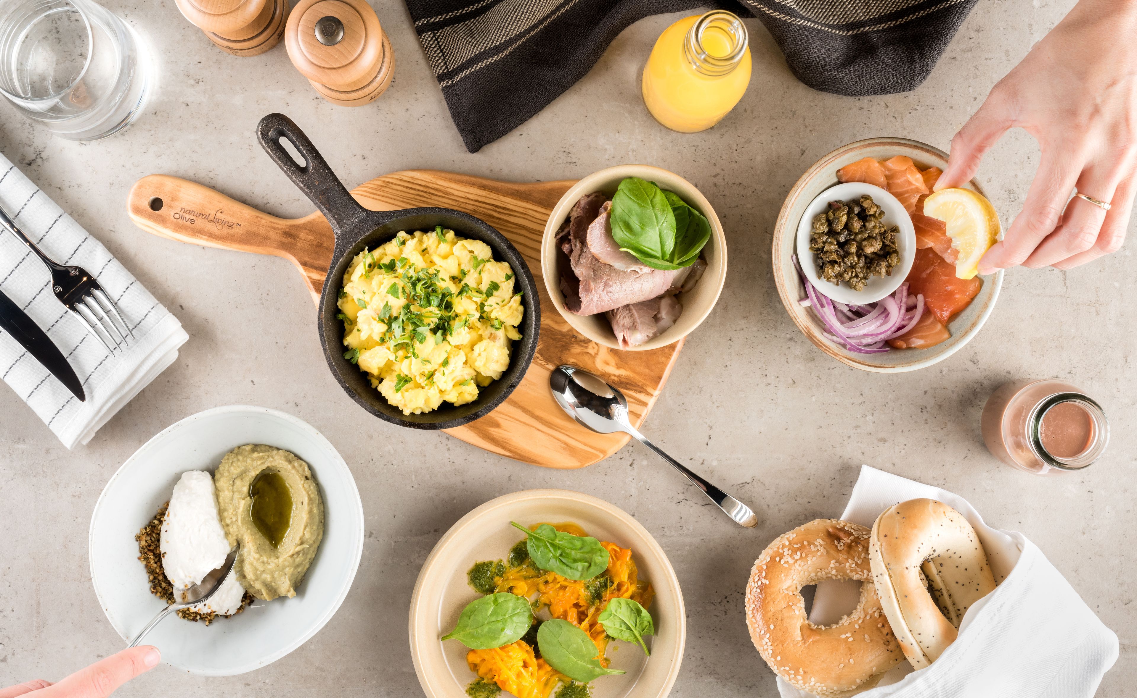 Ein Frühstückstisch mit Rührei, Schinken, Lachs, Bagels und verschiedenen Beilagen.
