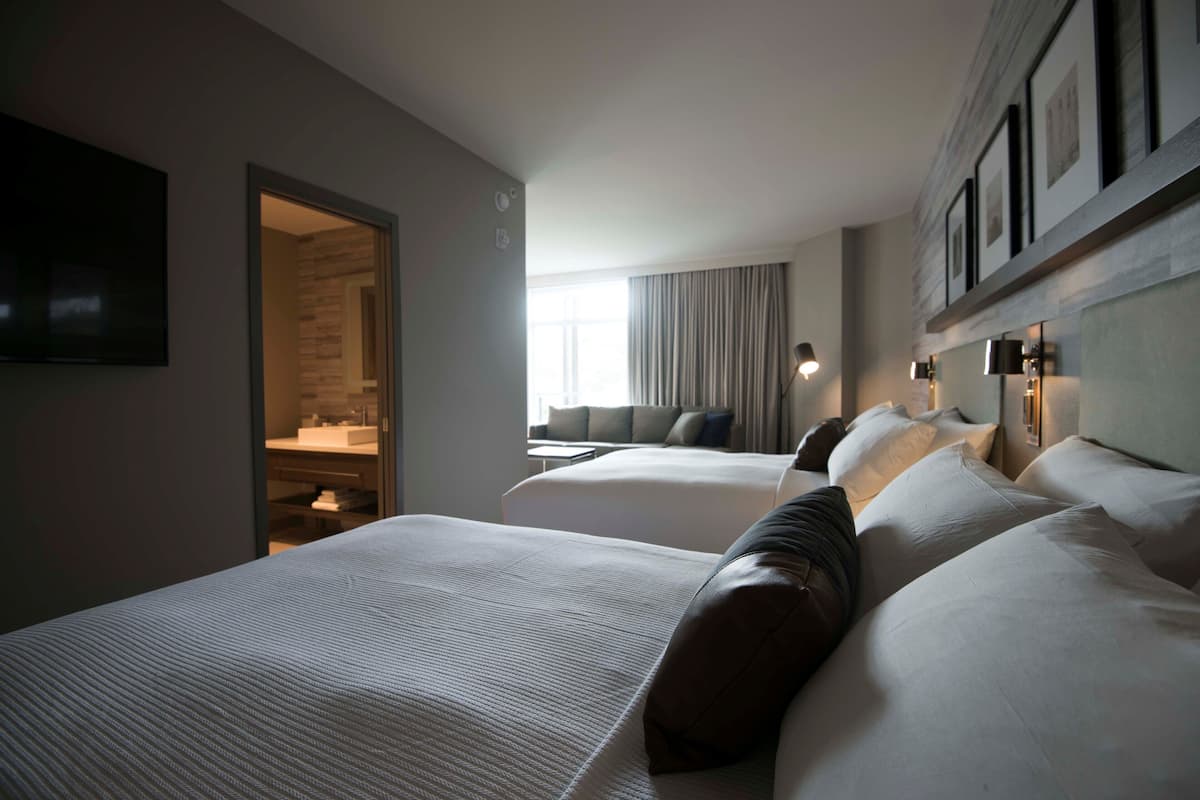 Une chambre d’hôtel avec deux lits, un dressing, une grande fenêtre avec des rideaux et des lampes fixées au mur.