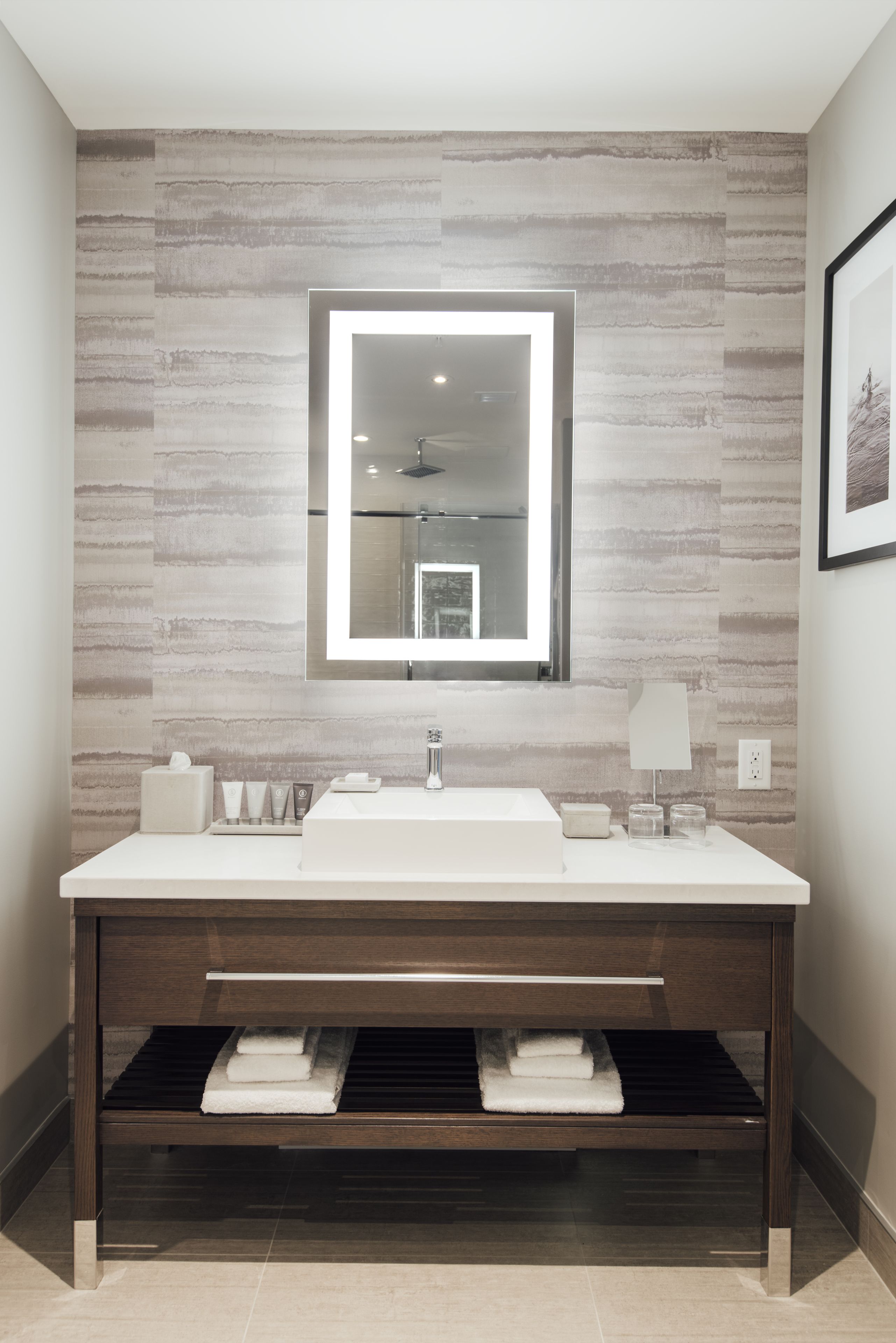 A modern bathroom with a large mirror, white sink, and dark wood vanity.