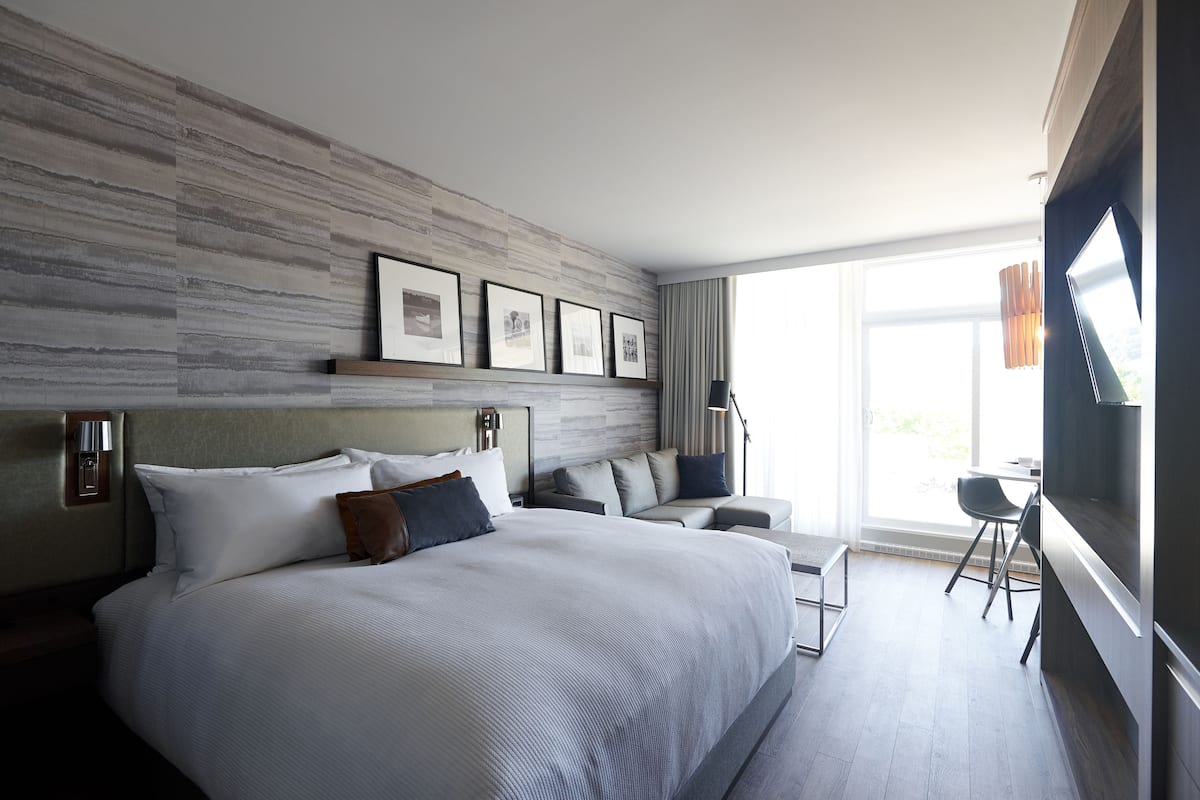 Une chambre d’hôtel moderne avec un grand lit, un canapé, un bureau et une grande fenêtre.