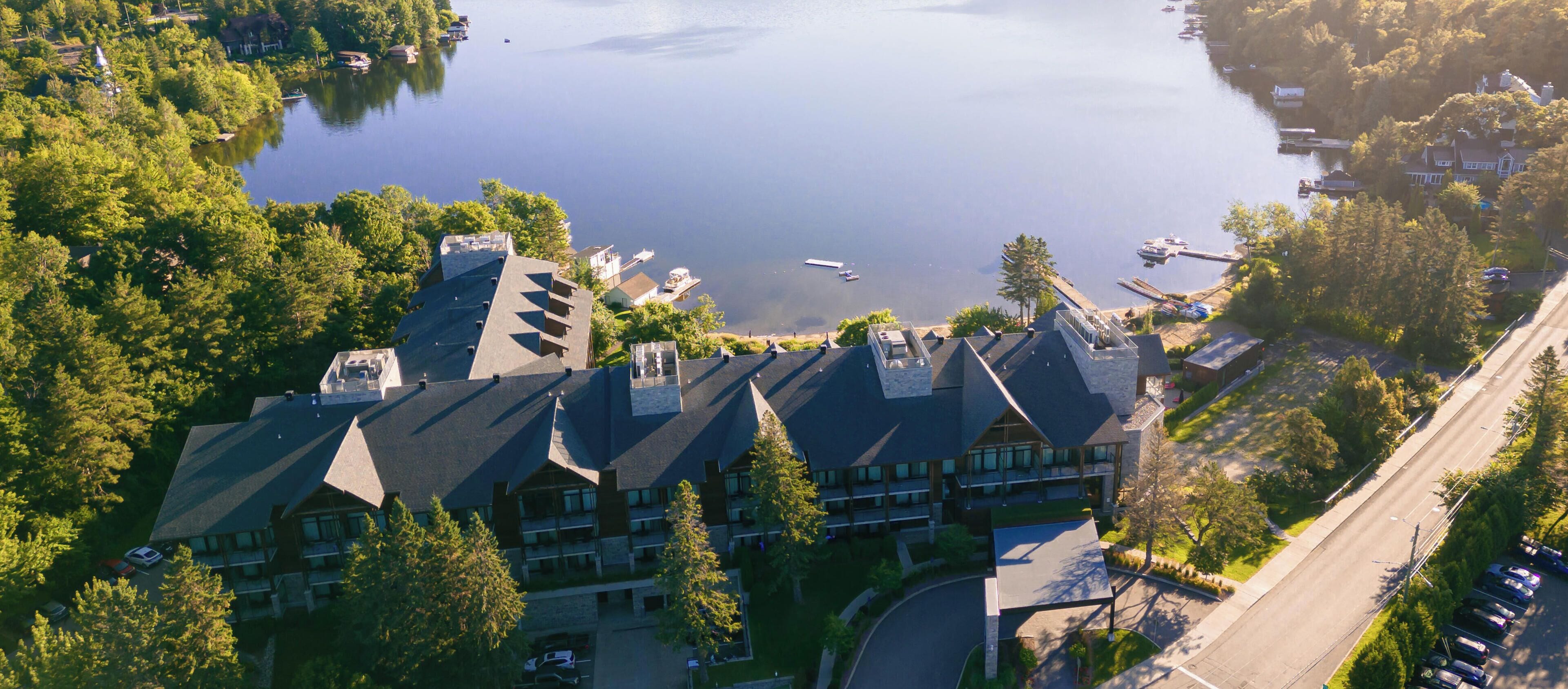 An aerial view of a hotel with multiple buildings, a parking lot, and a lake with boats.