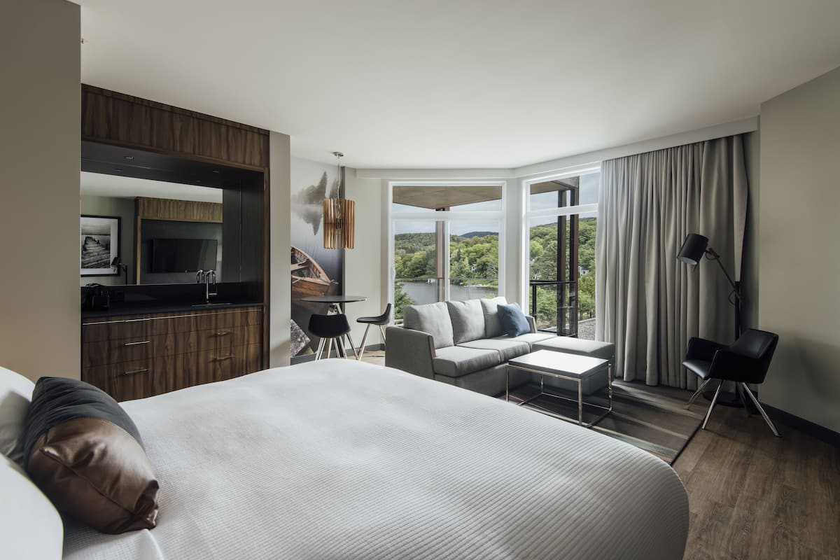 Une chambre d’hôtel moderne dotée d’un grand lit, d’un canapé, d’une petite table, d’une télévision et d’un balcon avec des rideaux.