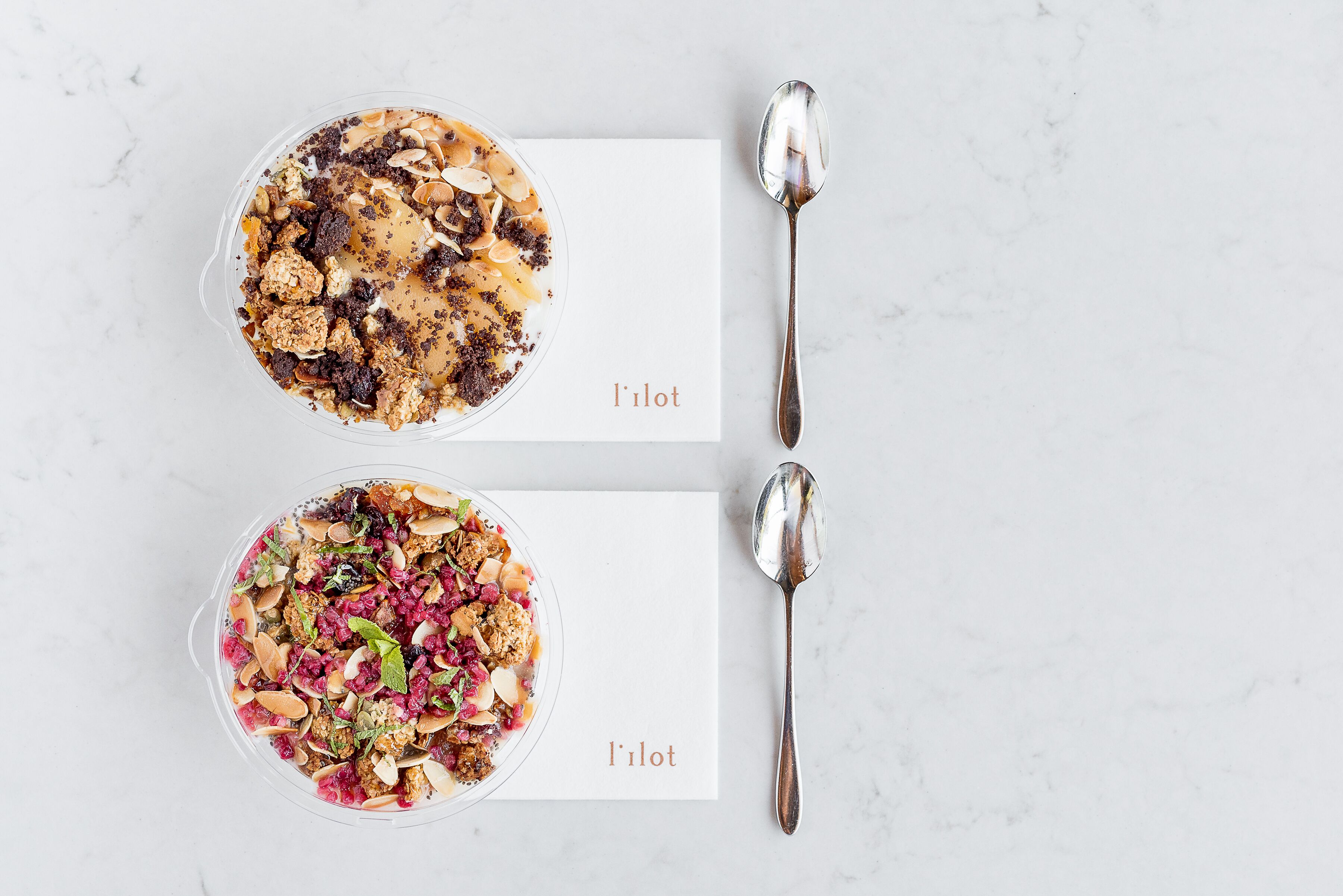 Dos tazones de granola con almendras y frutas secas sobre una superficie de mármol, con cucharas a un lado.