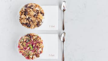 Dos tazones de granola con almendras y frutas secas sobre una superficie de mármol, con cucharas a un lado.
