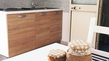 Una cocina con armarios de madera, una estufa y una ventana con vistas. Hay dos frascos con tapa sobre una mesa.