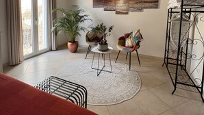 A well-lit room with a large window, a bed, a seating area with a table and chairs, and a wall-mounted artwork. - Nenetta Rooms (Monopoli)