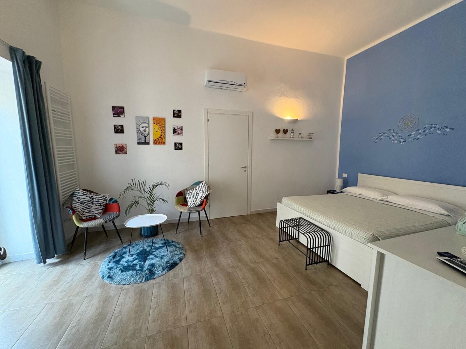 Una habitación compacta con una cama, una mesita pequeña, dos sillas y un aire acondicionado instalado en la pared.
