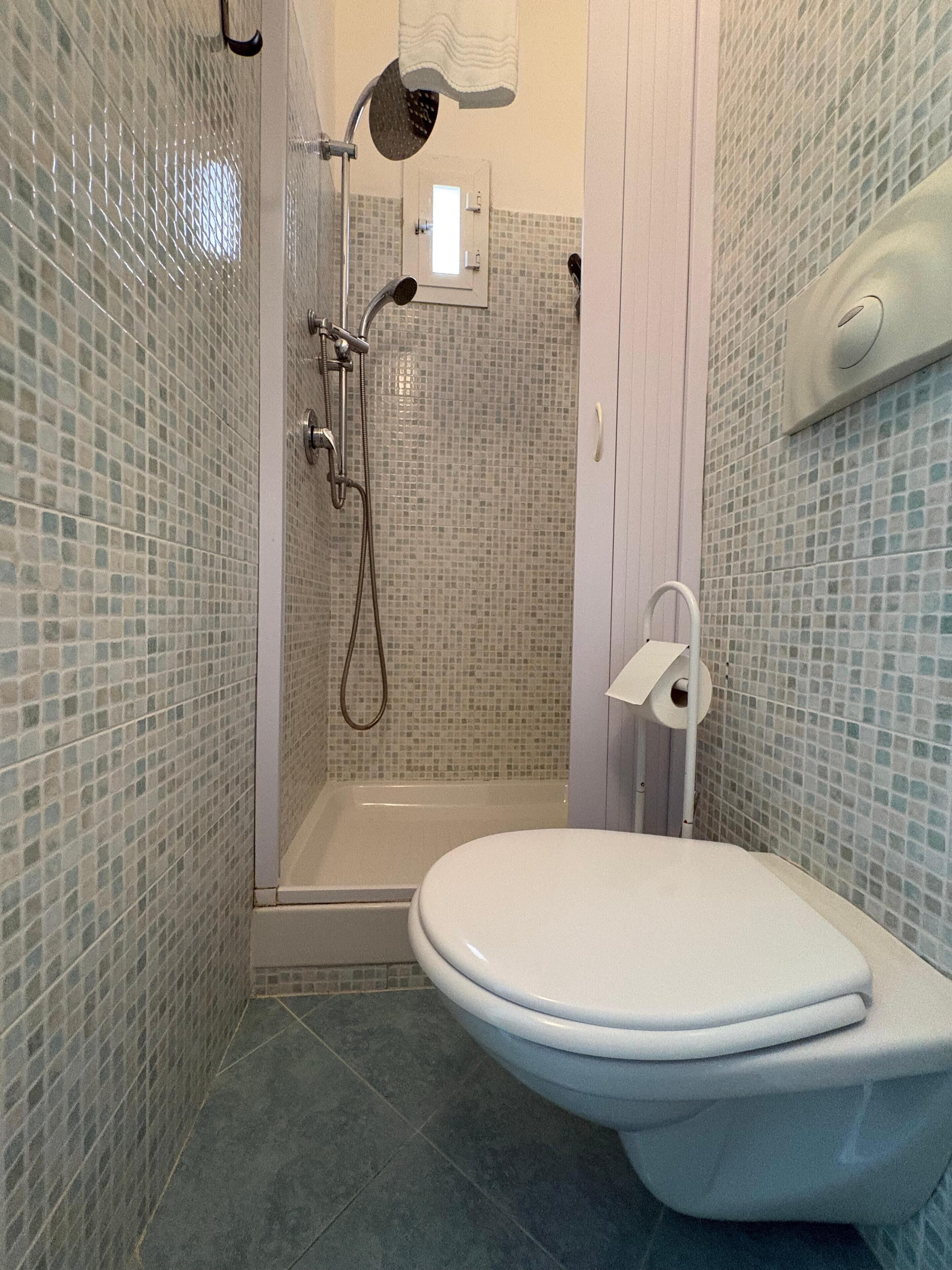 Un baño con ducha, inodoro y pared de azulejos.