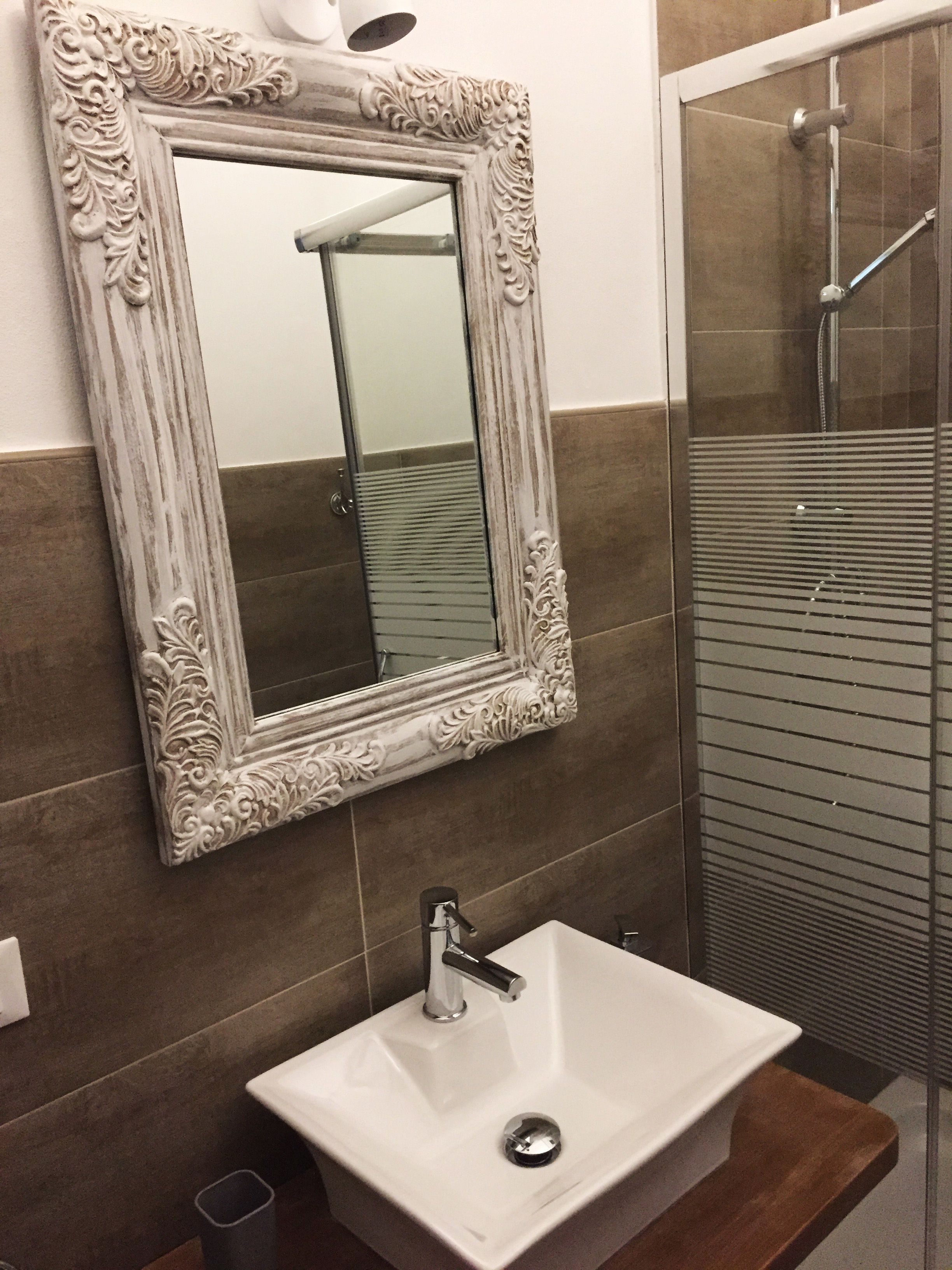 Une salle de bain avec un lavabo blanc, un miroir doté d’un cadre orné et un espace douche.