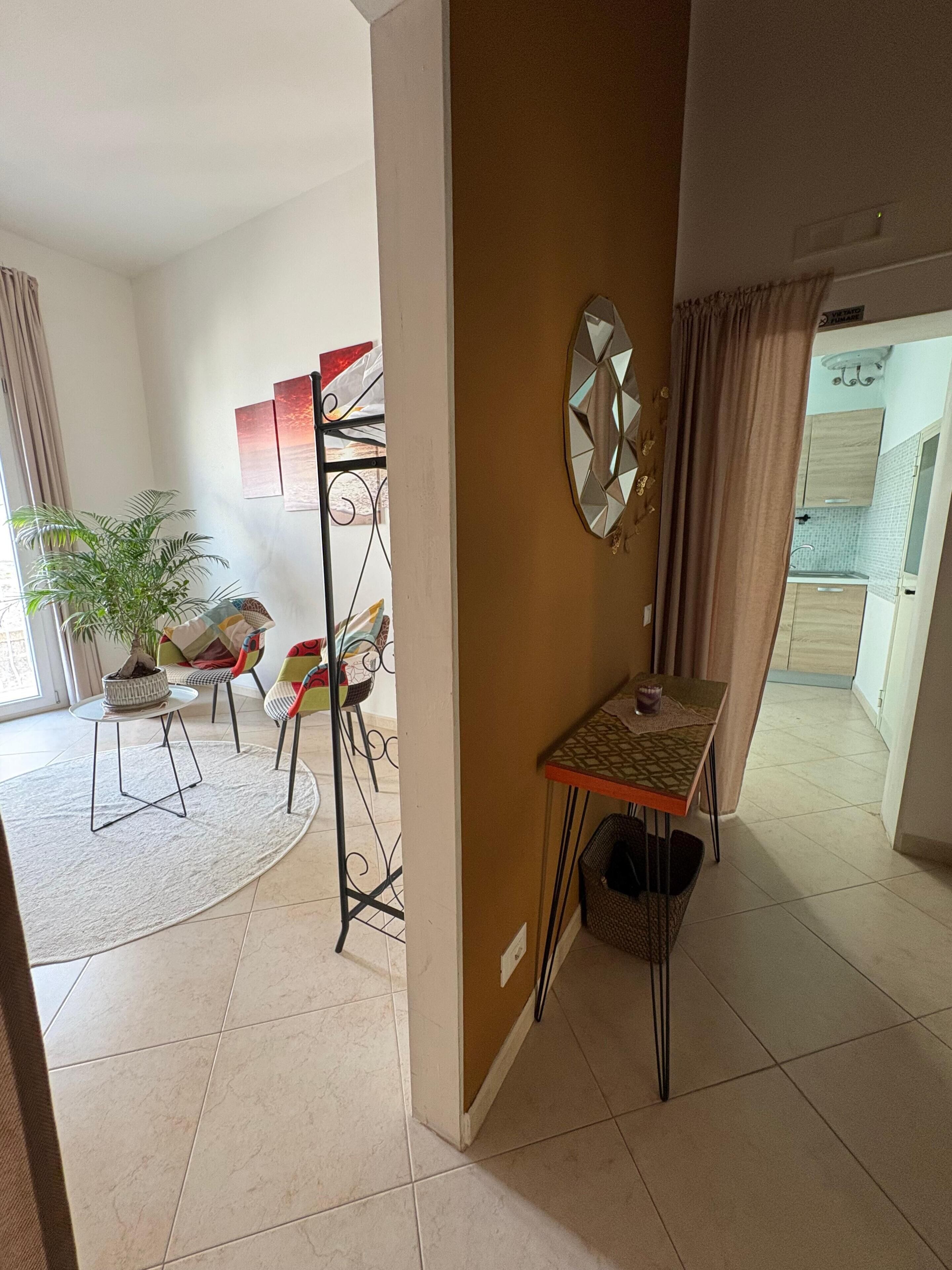 Una sala de estar amplia con un gran ventanal, un comedor con mesa y sillas, una planta en maceta y un espejo decorativo en la pared.