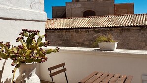 A terrace with a white wall, a cactus plant, a wooden bench, a table, and a view of a historical building with a dome. - Nenetta Rooms (Monopoli)