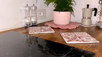 A kitchen counter with a black induction cooktop, a potted plant, salt and pepper shakers, a coffee maker, and decorative coasters.