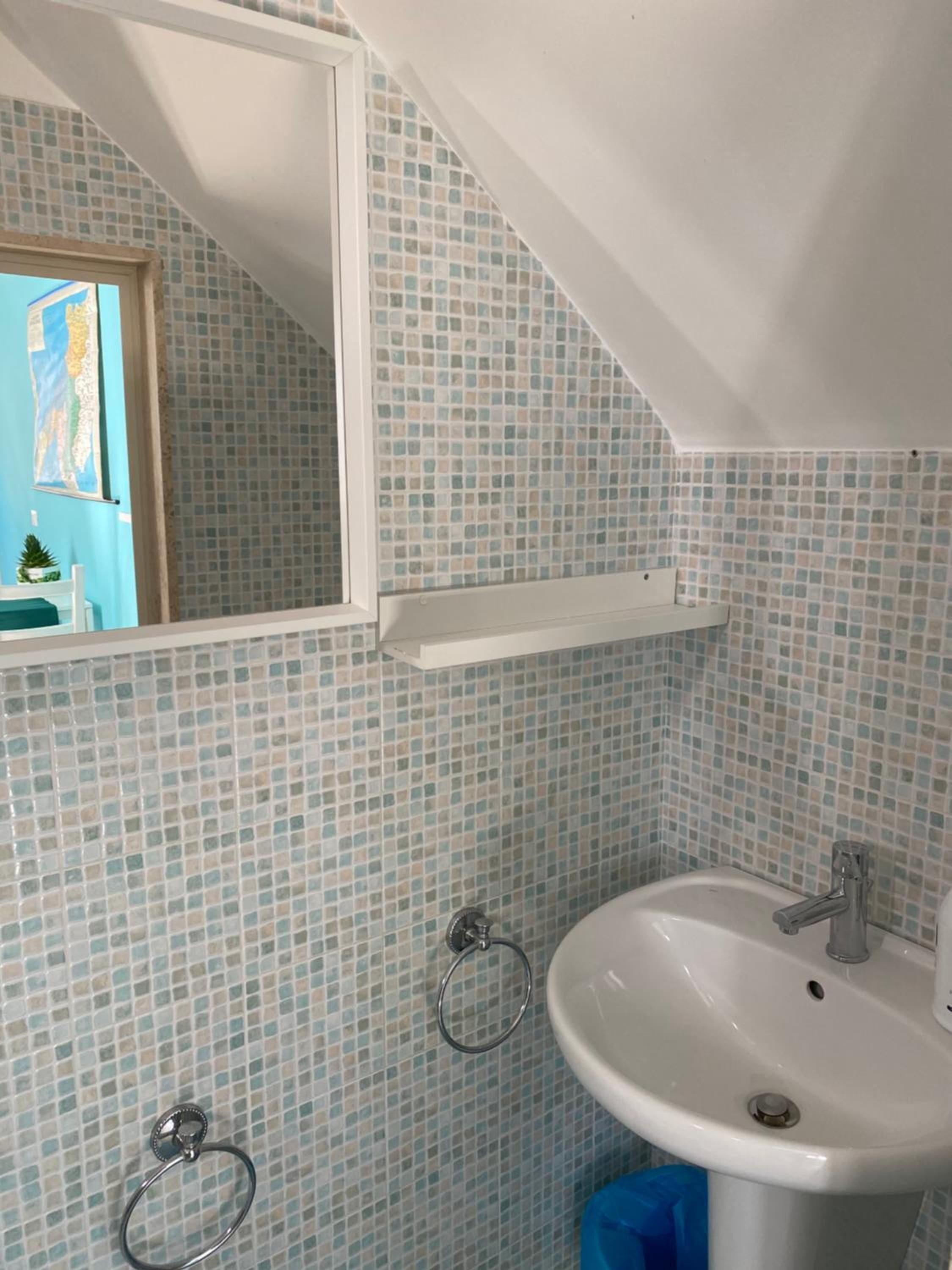 Un baño con un lavamanos blanco, un espejo y paredes con azulejos.