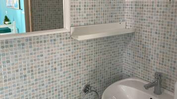Un baño con un lavamanos blanco, un espejo y paredes con azulejos.