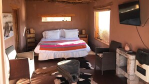 Un dormitorio rústico con una cama, un televisor, una chimenea de piedra y una alfombra de cuero de vaca.