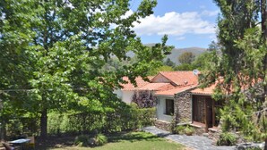 A stone house with a tiled roof, surrounded by lush greenery and a well-maintained lawn.