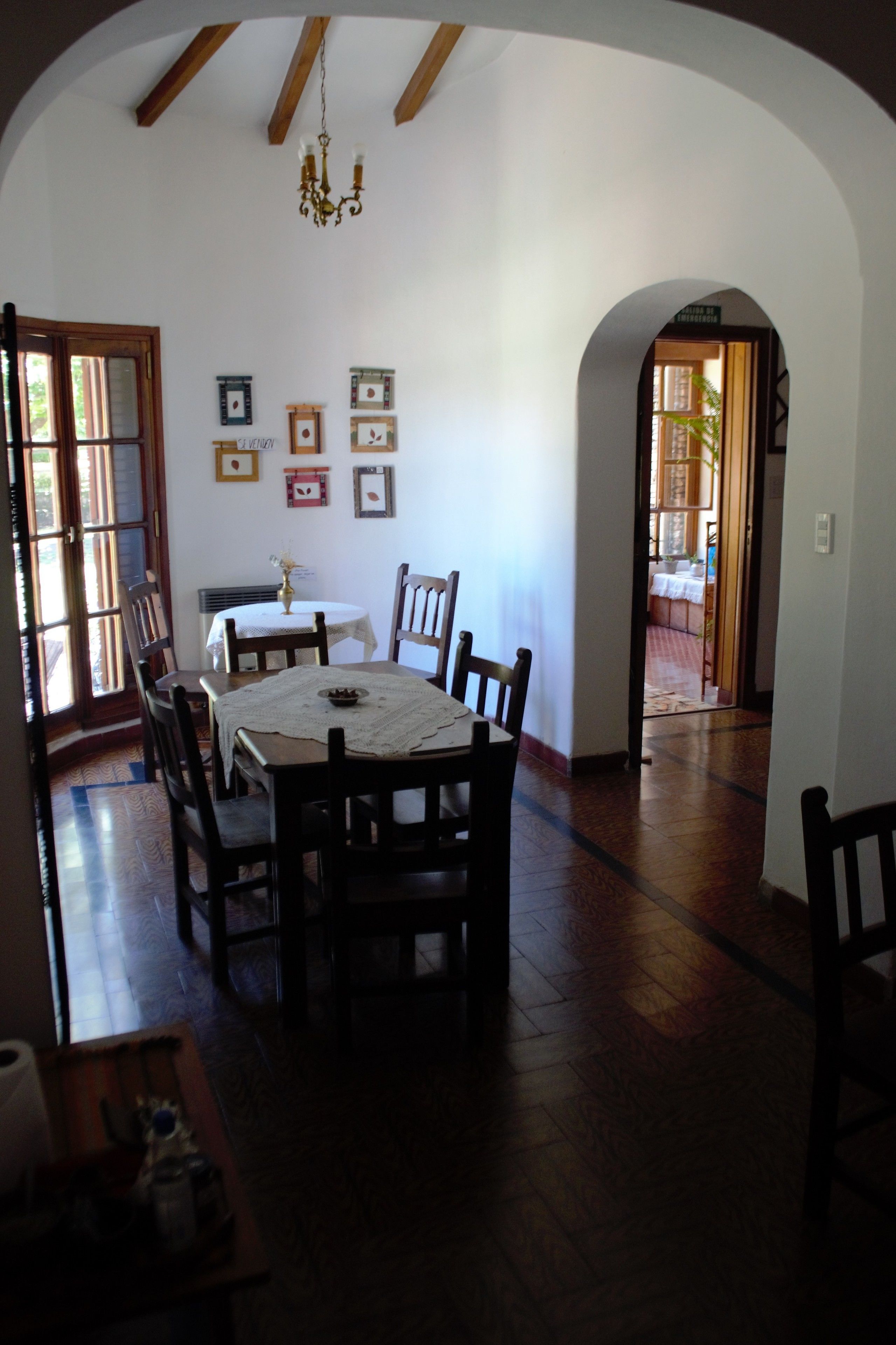 Un comedor con una mesa redonda, sillas de madera y una araña. Hay cuadros en la pared y una puerta que da a otra habitación.