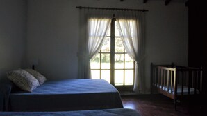 A room with a large window, a bed with a headboard, and a wooden crib.