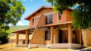 A two-story brick house with a covered patio and a staircase leading to the upper floor. - Pasárgada Hotel (Crato)