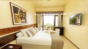 A hotel room with a bed, a TV, a painting, and a balcony with curtains. - Pasárgada Hotel (Crato)