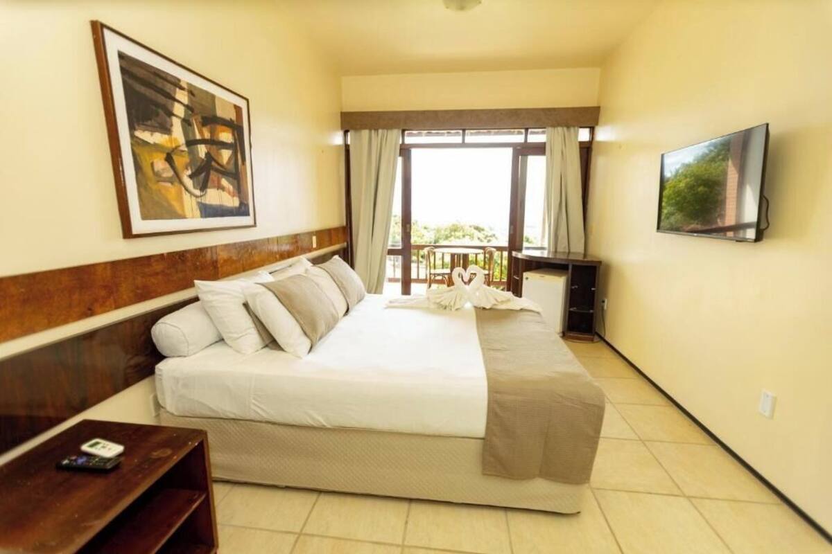 A hotel room with a bed, a TV, a painting, and a balcony with curtains.