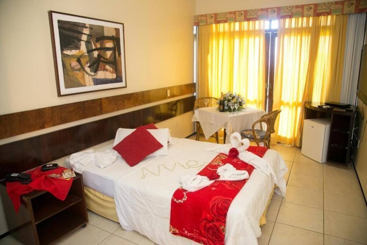 A hotel room with a bed, a desk, a chair, a small table, and a television.