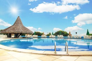 Una piscina con sillones de descanso y una estructura de techo de paja.