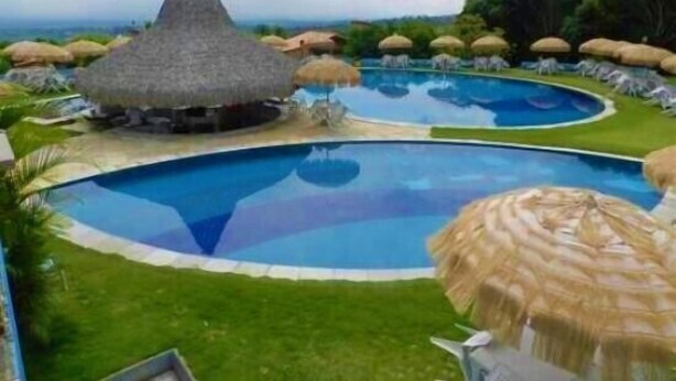 A swimming pool with a thatched-roof structure and lounge chairs. - Pasárgada Hotel (Crato)