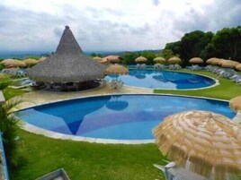 Una piscina con una estructura de techo de paja y sillones de descanso.