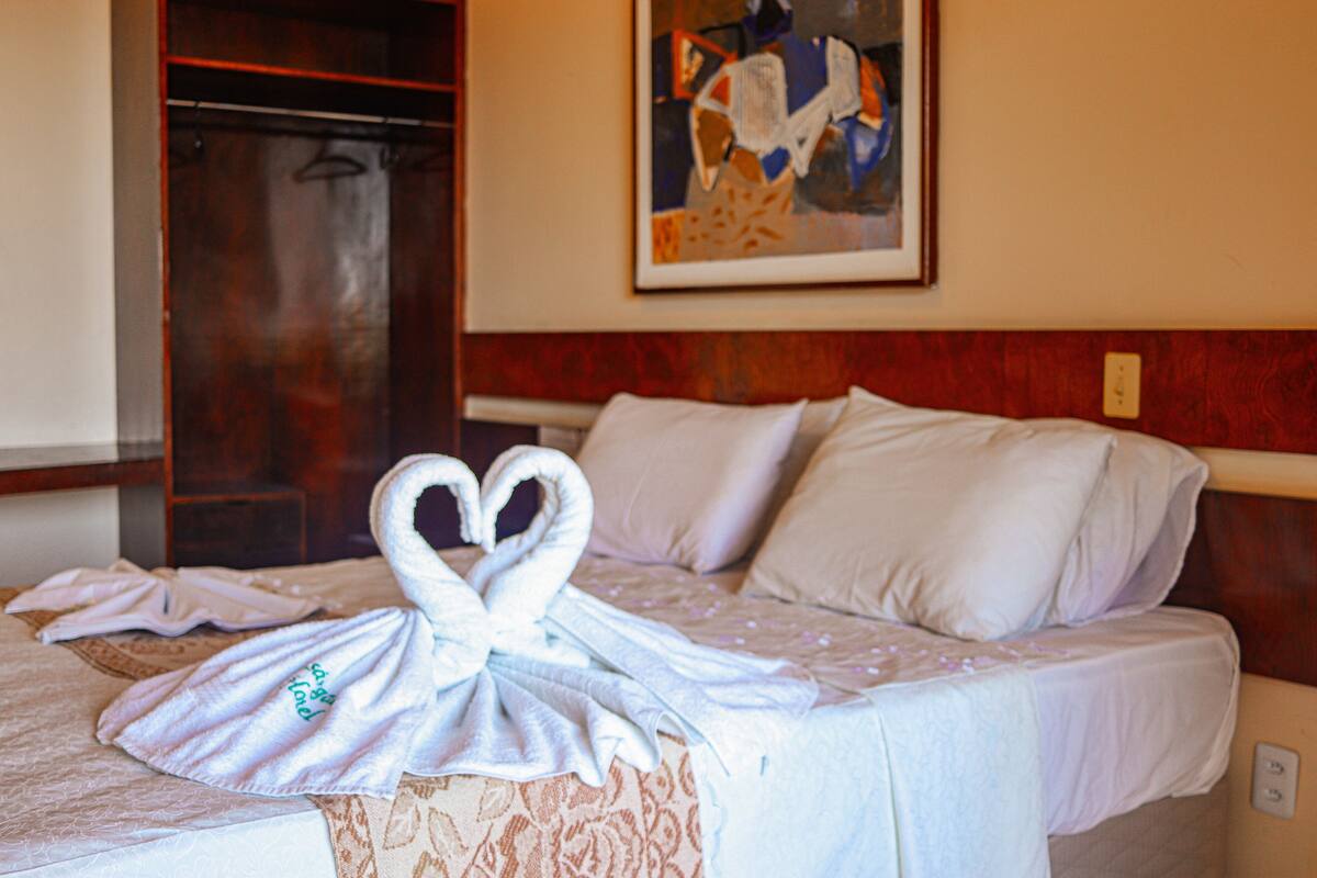 A hotel room with a bed, a towel art arrangement, a painting on the wall, and a wooden headboard.