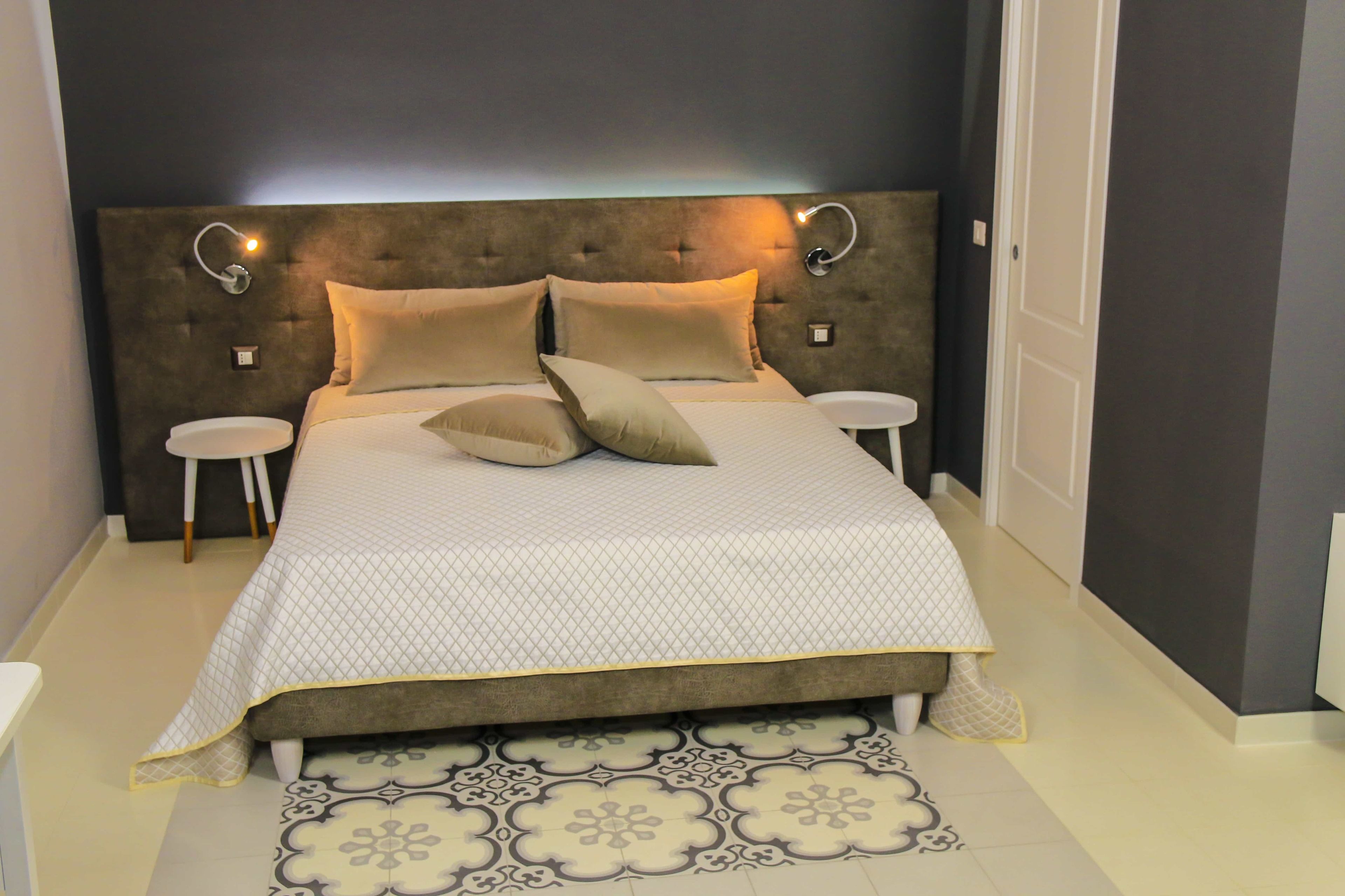 A bedroom with a tufted headboard, two bedside tables, a patterned rug, and a neutral color scheme.