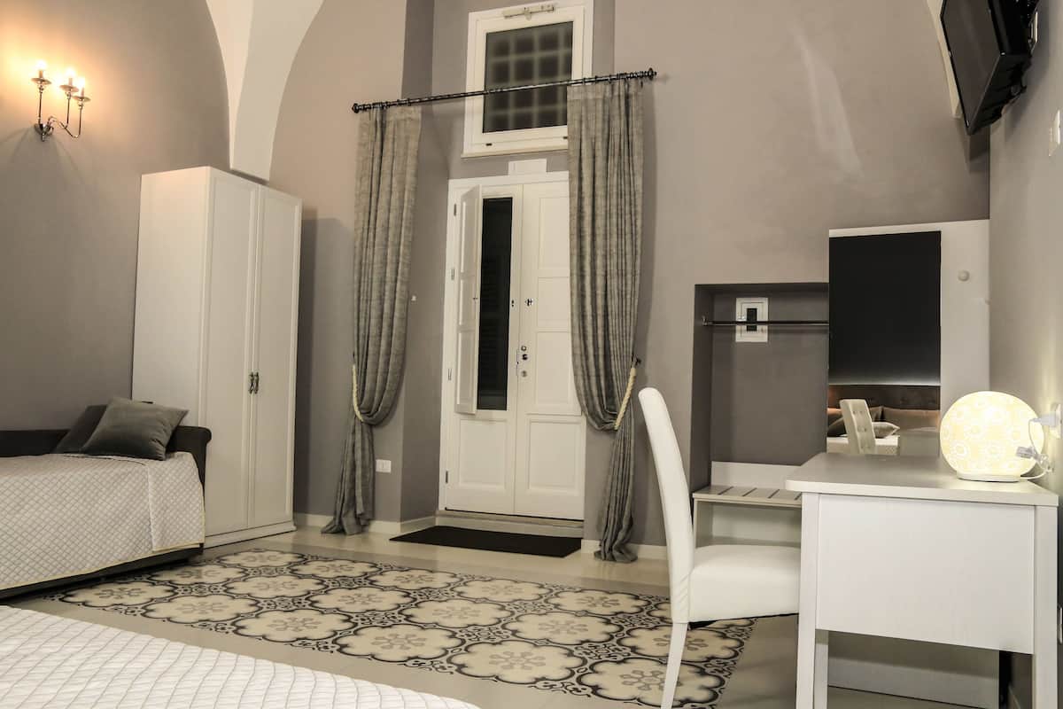 Ein Schlafzimmer mit Bett, Schreibtisch, Lampe, Kleiderschrank und einer Tür mit Vorhängen.