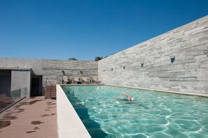 Una piscina interior con agua cristalina, rodeada de paredes de piedra y una terraza de madera.