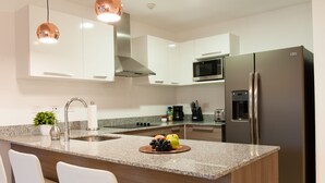 A modern kitchen with a stainless steel refrigerator, a microwave, and a sink. There are two white bar stools and a potted plant on the counter. - Splendor Stay Escalante (Mercedes)