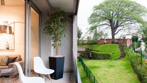 A modern living room with a sofa, chairs, and a large window overlooking a well-maintained garden with a tree and a brick wall. - Splendor Stay Escalante (Mercedes)