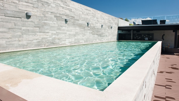 A rectangular pool with clear water, surrounded by a light-colored wall and a wooden deck. - Splendor Stay Escalante (Mercedes)