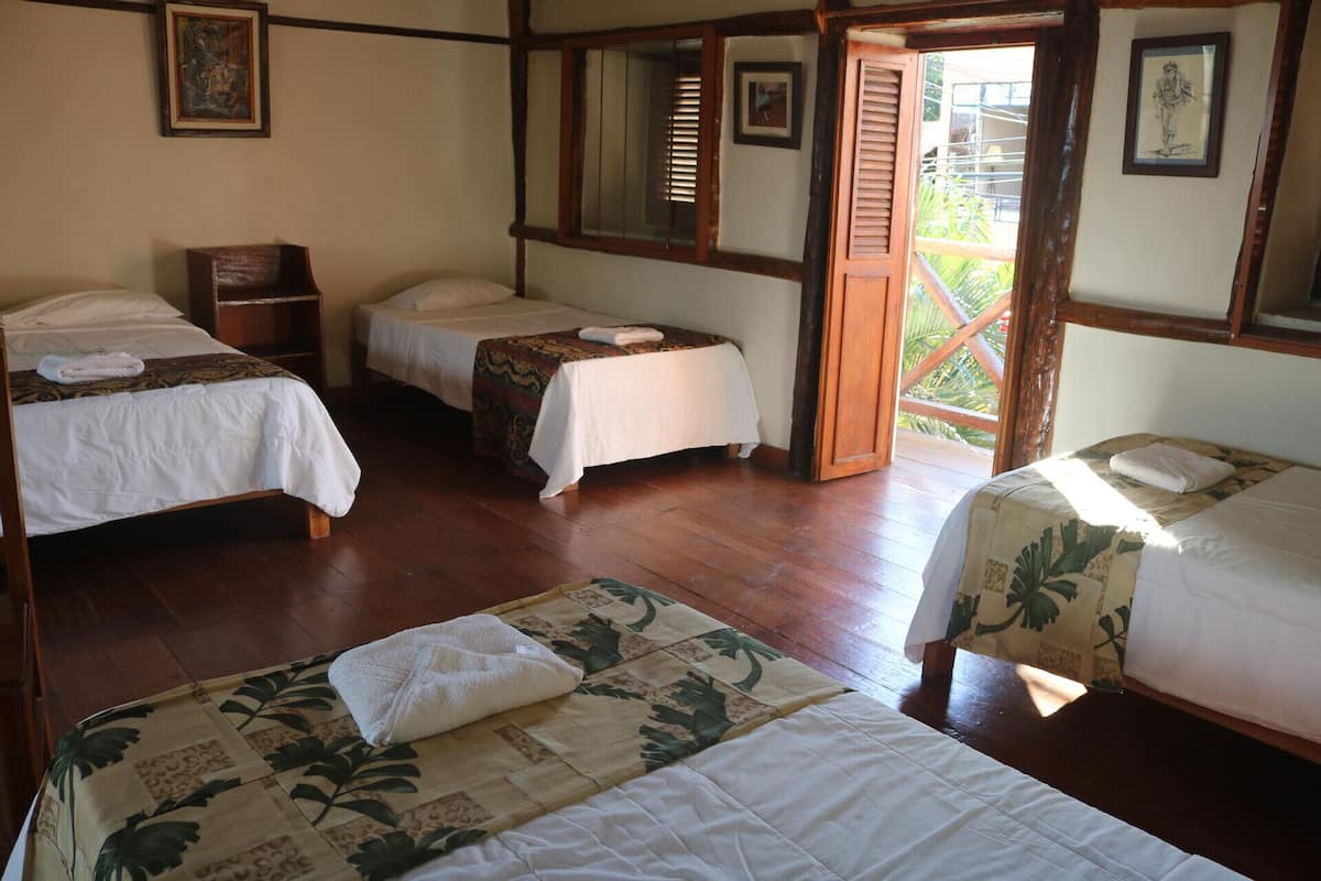 Une chambre avec trois lits simples, un plancher en bois et une grande fenêtre avec des stores.