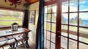 A wooden interior with a table and bench, a door with glass panels, and a view of the outdoors.