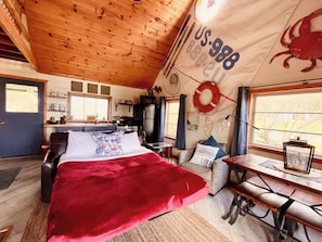 Un interior de cabaña acogedor con una cama grande, una mesa de comedor y una zona de cocina.