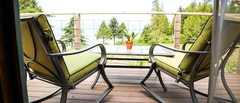 Ein Balkon mit zwei Schaukelstühlen und einem kleinen Tisch, der auf eine Holzterrasse und viel Grün blickt.