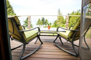 Een balkon met twee schommelstoelen en een tafeltje, met uitzicht op een houten terras en groen.