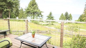 A deck with a table and chairs, overlooking a fenced yard with trees and a view of the water.