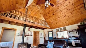 A cozy cabin interior with a loft bedroom, a living room with a fireplace, and a kitchen area.