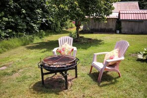 A backyard with a grill and two Adirondack chairs with floral cushions.