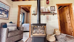 A cozy room with a wood-burning stove, a sofa, a bed, and a wooden ceiling.